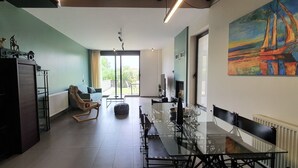 A modern living room with a glass dining table, a sofa, and a painting of a sailboat.