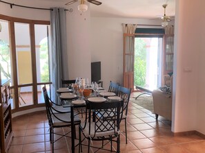 A dining area with a table set for four, chairs, a television, and a view of greenery outside.