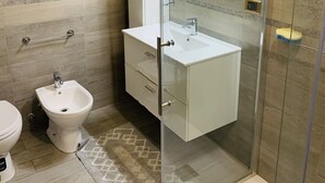 Un baño moderno con ducha envuelta en vidrio, un lavabo blanco y un bidé.