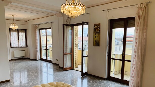 Una habitación amplia con piso de mármol, sofá capitonado, candelabro y ventanas grandes con cortinas.