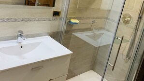 Un baño con ducha de vidrio, lavabo blanco y mueble de madera.