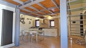 Una cucina moderna con mobili bianchi, un'area pranzo con tavolo e sedie e una scala con ringhiera in vetro.