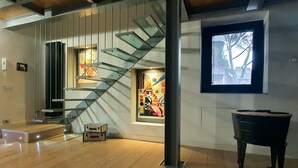 Un interno moderno con pavimento in legno, una scala con gradini in vetro, un pianoforte e arte astratta alle pareti.