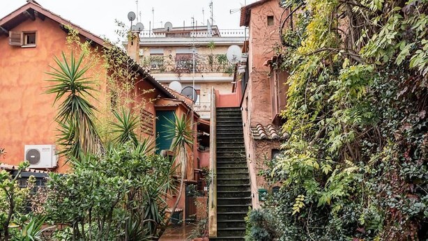 Un stretto vicolo con una scala che conduce a un edificio con facciata rossa.