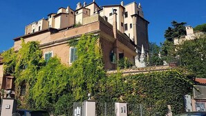 Un edificio storico con una torre imponente, mura coperte d'edera e un ingresso con cancello.