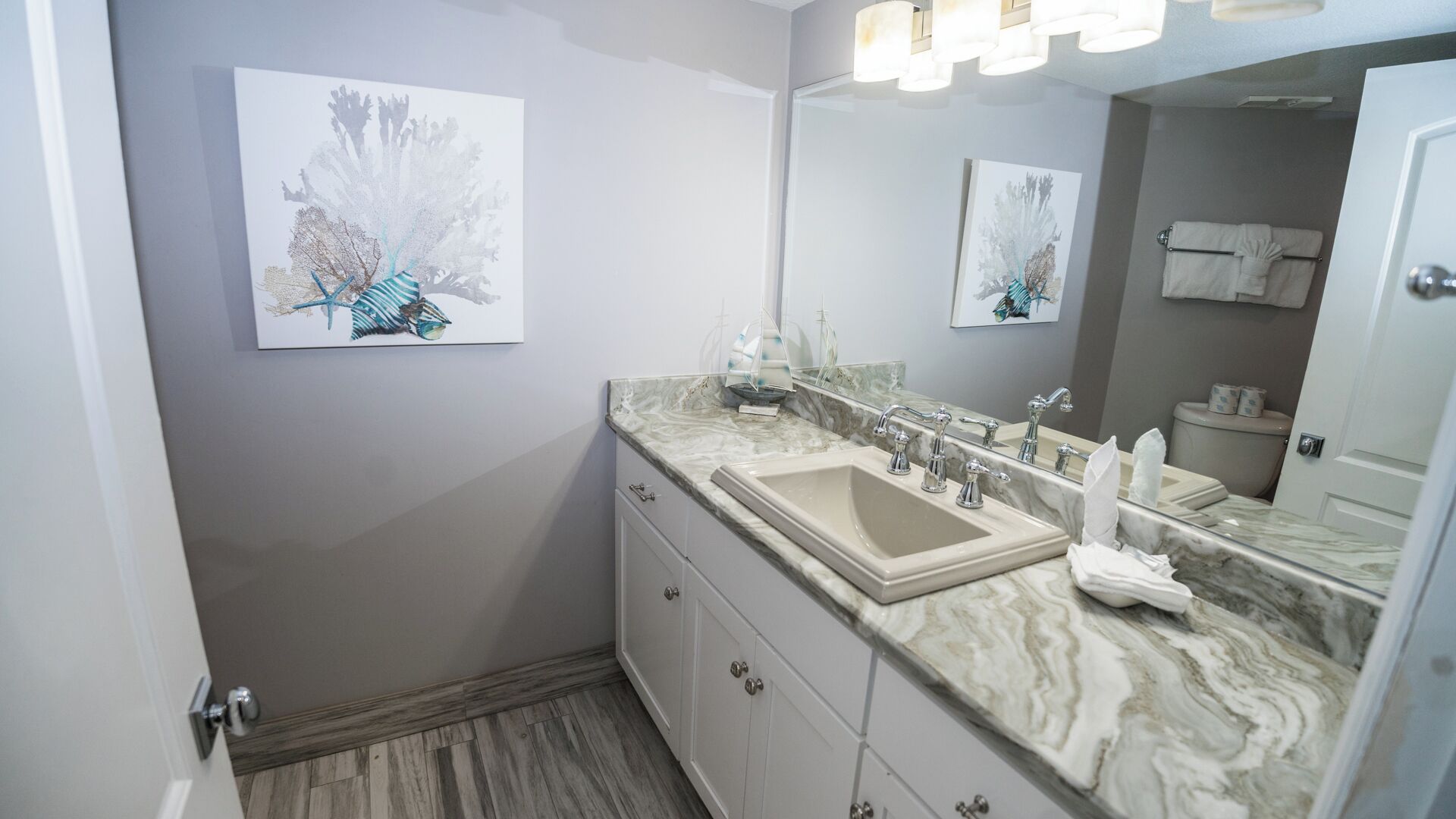 A bathroom with a marble countertop, a sink, a mirror, and artwork on the wall.