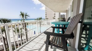 Un balcón con vistas a una piscina y una playa, una mesa y una silla.
