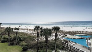 Vista de una playa con palmeras, una zona de piscina con sombrillas y un cielo despejado.