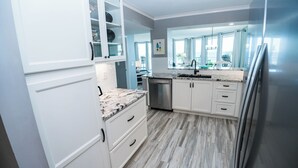 Una cocina moderna con armarios blancos, una encimera de granito y un refrigerador de acero inoxidable.