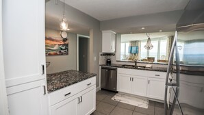 A modern kitchen with white cabinets, granite countertops, stainless steel appliances, and a large window with a view. - E1101 Gulf Front, Amazing View, 3 Pools, Gated Condo (Panama City)