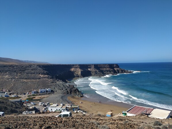 A coastal area with rocky terrain, a beach, and a cliff overlooking the ocean. - Family Heaven (El Cotillo, Fuerteventura)