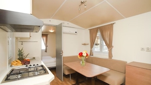 A compact kitchen with a gas stove, a sink, and a dining area with a table and bench. - Mediteran Travel Mobile Homes Basko Polje (Baska Voda)