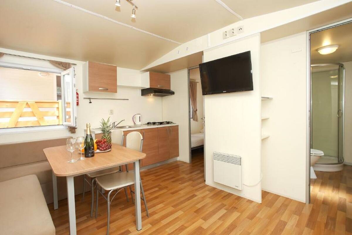 A compact kitchen with a dining area, a TV mounted on the wall, and a shower area.