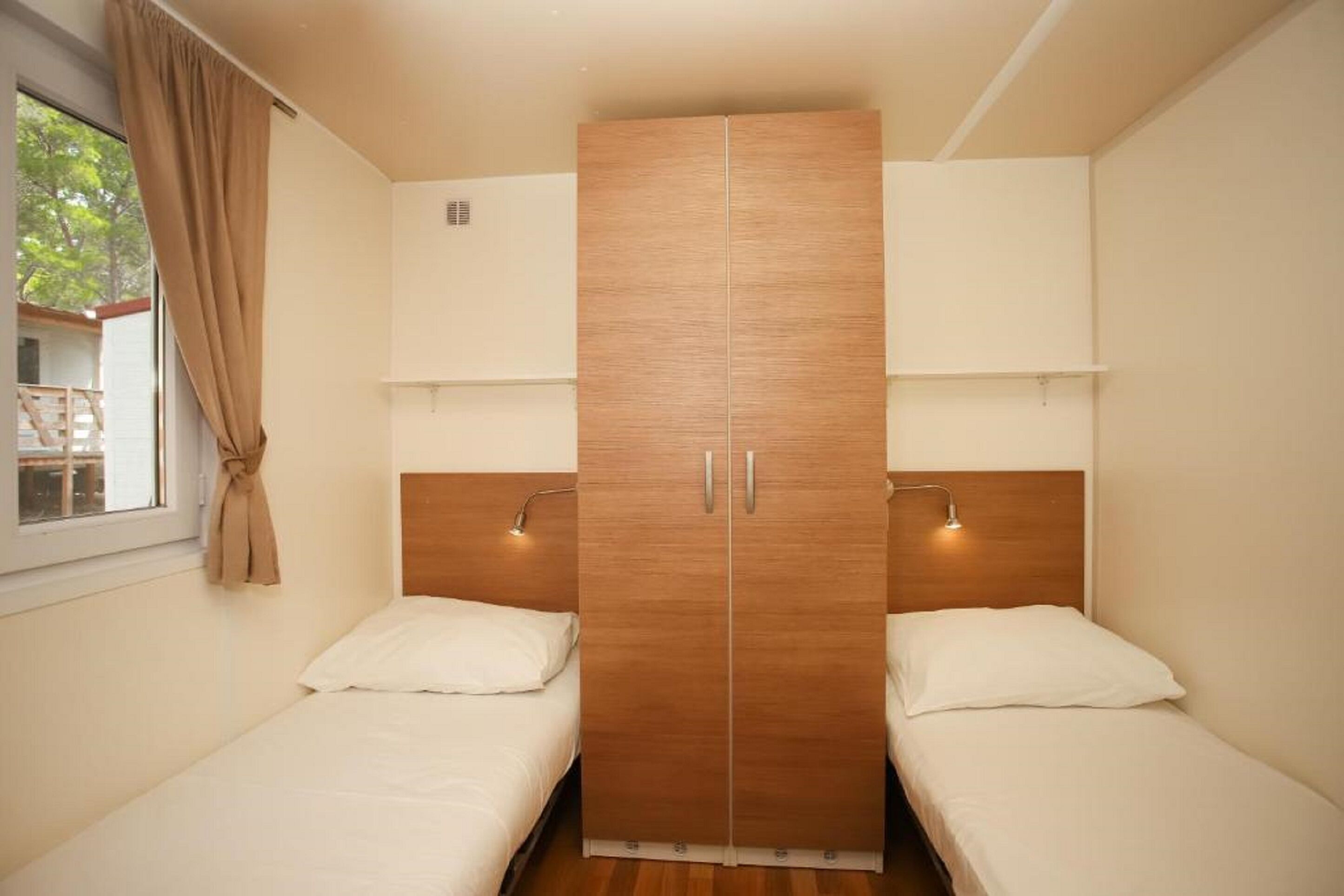 Ein Schlafzimmer mit zwei Einzelbetten, einem Holzschrank und einem Fenster mit Vorhängen.