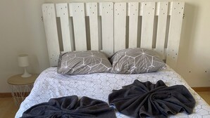 Una cama con una colcha de diseño geométrico, dos almohadas con un diseño similar y dos toallas oscuras dispuestas sobre la cama.
