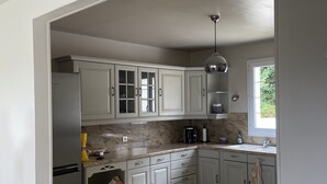 Una cocina moderna con armarios blancos, un refrigerador de acero inoxidable, una encimera de mármol y una ventana que proporciona luz natural.