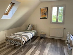 A bedroom with a sloped ceiling, a bed, a radiator, a window, and a picture on the wall.