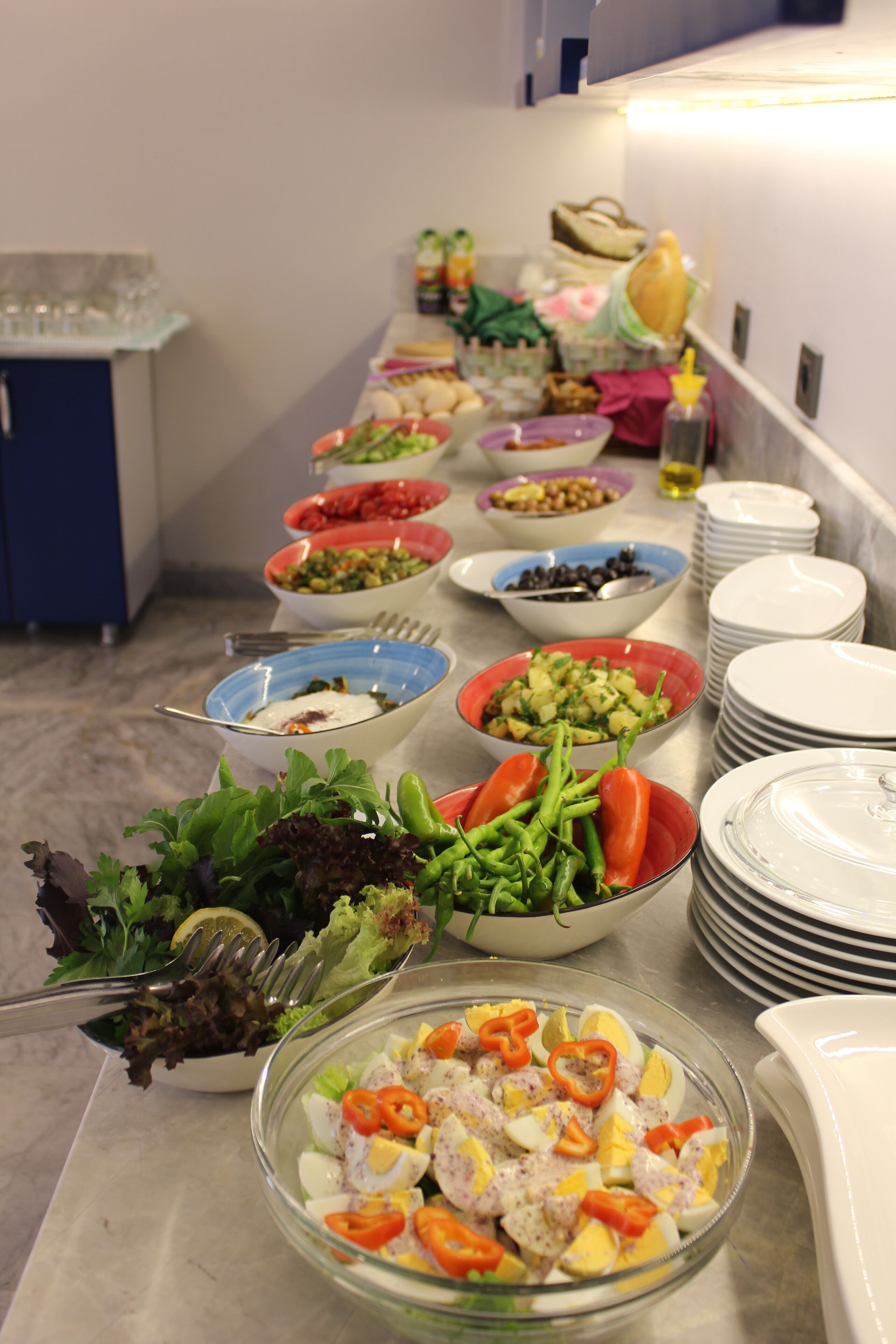 Una barra de buffet con diversos platos, incluyendo ensaladas, verduras y un tazón de huevos y pimientos.