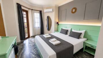 Habitación de hotel con cama, escritorio, espejo, aire acondicionado de pared y ventana con cortinas.
