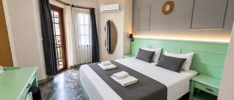 Habitación de hotel con cama, escritorio, espejo, aire acondicionado de pared y ventana con cortinas.
