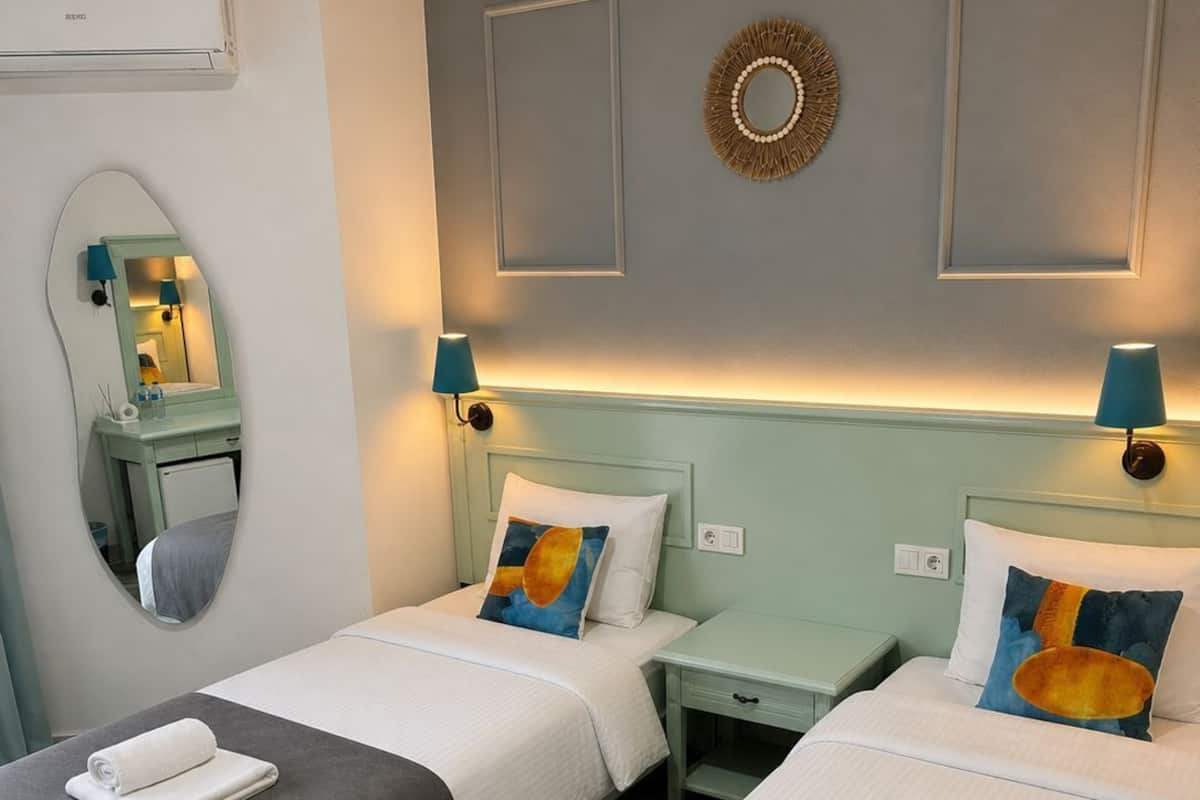 A hotel room with two beds, a mirror, a wall-mounted air conditioner, and two bedside lamps.