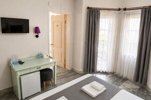 Habitación de hotel con escritorio, televisión, puerta y ventana con cortinas.
