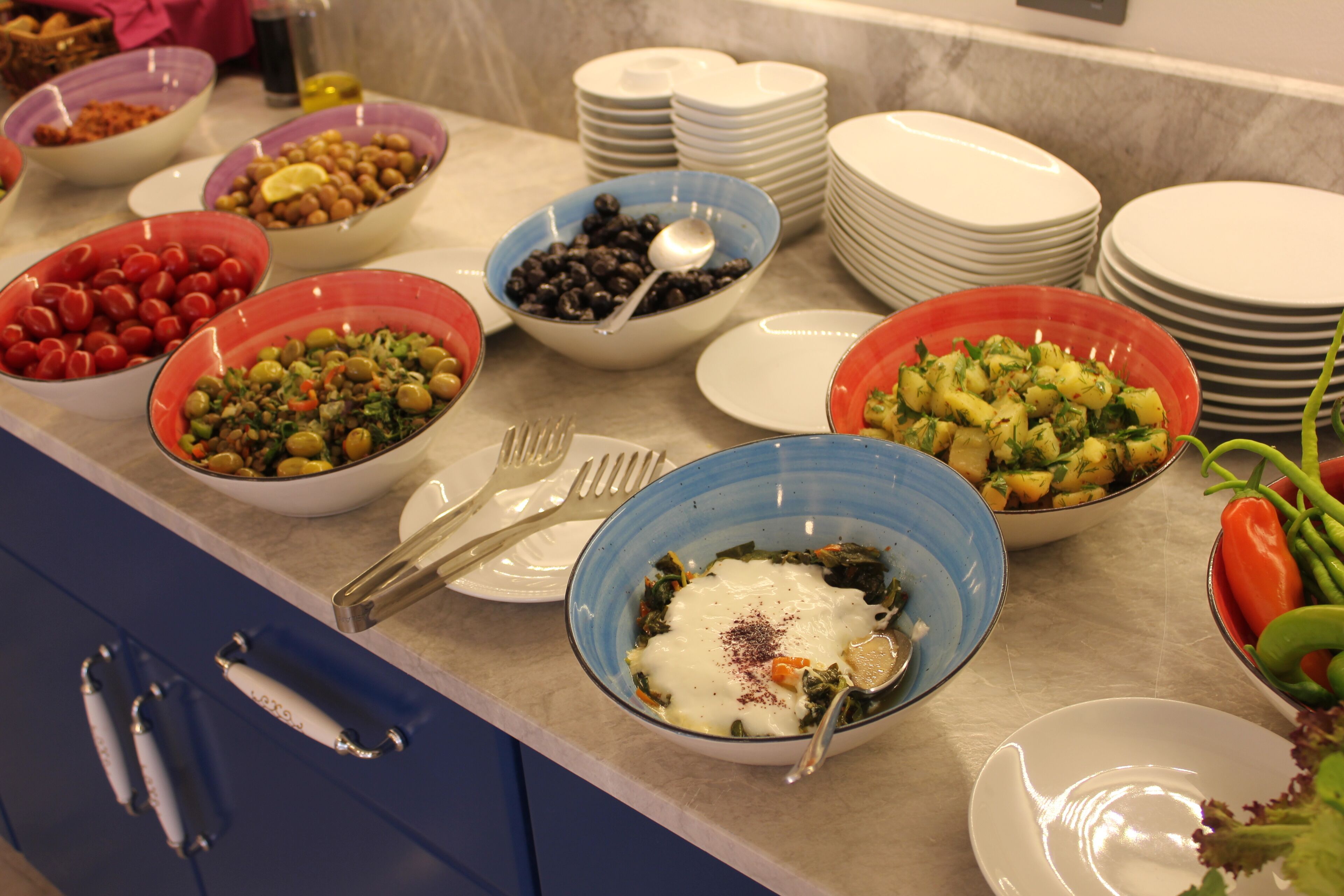 Une table de buffet présentant divers plats et des saladiers remplis de nourriture, notamment des salades et des haricots, disposés sur un comptoir en marbre.