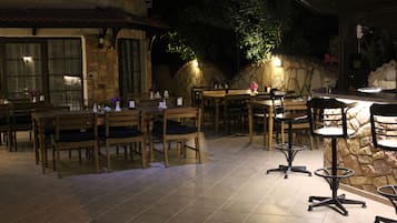 Un espace extérieur aménagé pour les repas, avec des tables et des chaises en bois, des murs en pierre et des plantes en pot.