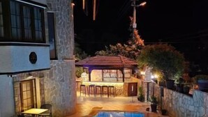 A swimming pool with a stone wall and a bar area in the background. - Gokova Hotel (Ula)