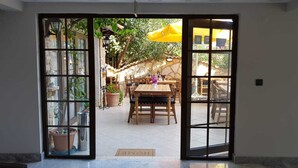A doorway leading to an outdoor patio with a wooden table and chairs, surrounded by potted plants and a yellow umbrella. - Gokova Hotel (Ula)