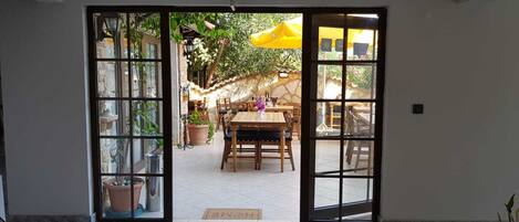 A doorway leading to an outdoor patio with a wooden table and chairs, surrounded by potted plants and a yellow umbrella.