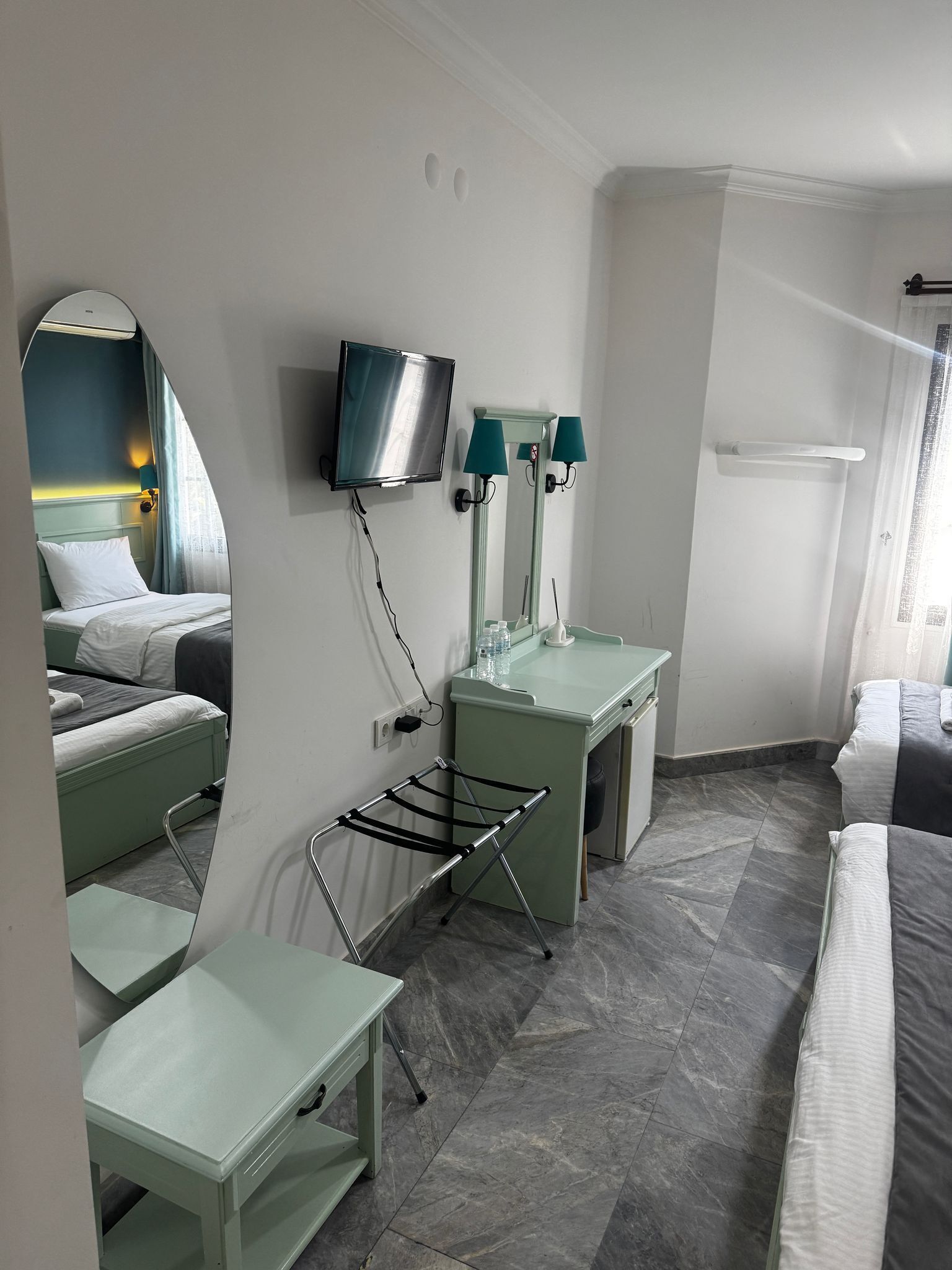 A hotel room with a bed, a desk, a mirror, a TV, and a bathroom area.
