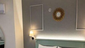 A neatly made bed with two pillows, a wall-mounted mirror, and a wall sconce. - Gokova Hotel (Ula)