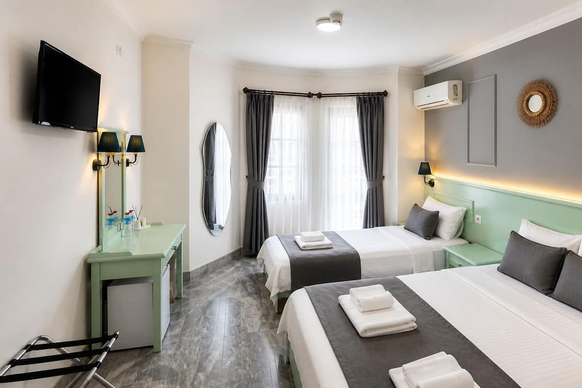 A hotel room with two beds, a TV, a desk, and a mirror.