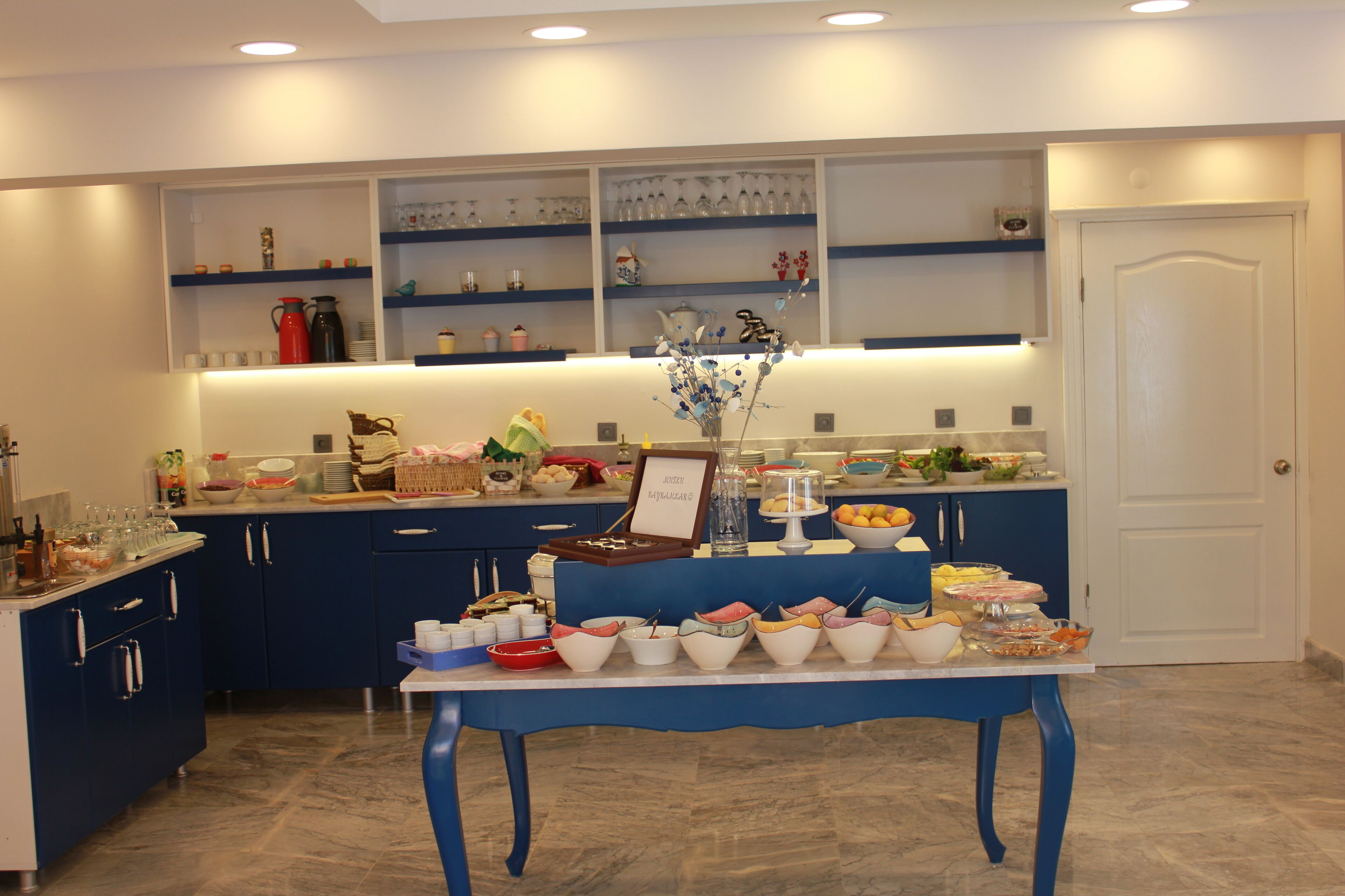 Una cocina con una disposición tipo bufé, que incluye una mesa con fuentes y un letrero.