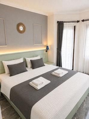 A neatly made bed with pillows, a bedside lamp, and a wall-mounted mirror. - Gokova Hotel (Ula)
