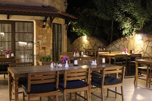 Ένας εξωτερικός χώρος για φαγητό με πέτρινους τοίχους, ξύλινα τραπέζια και καρέκλες.