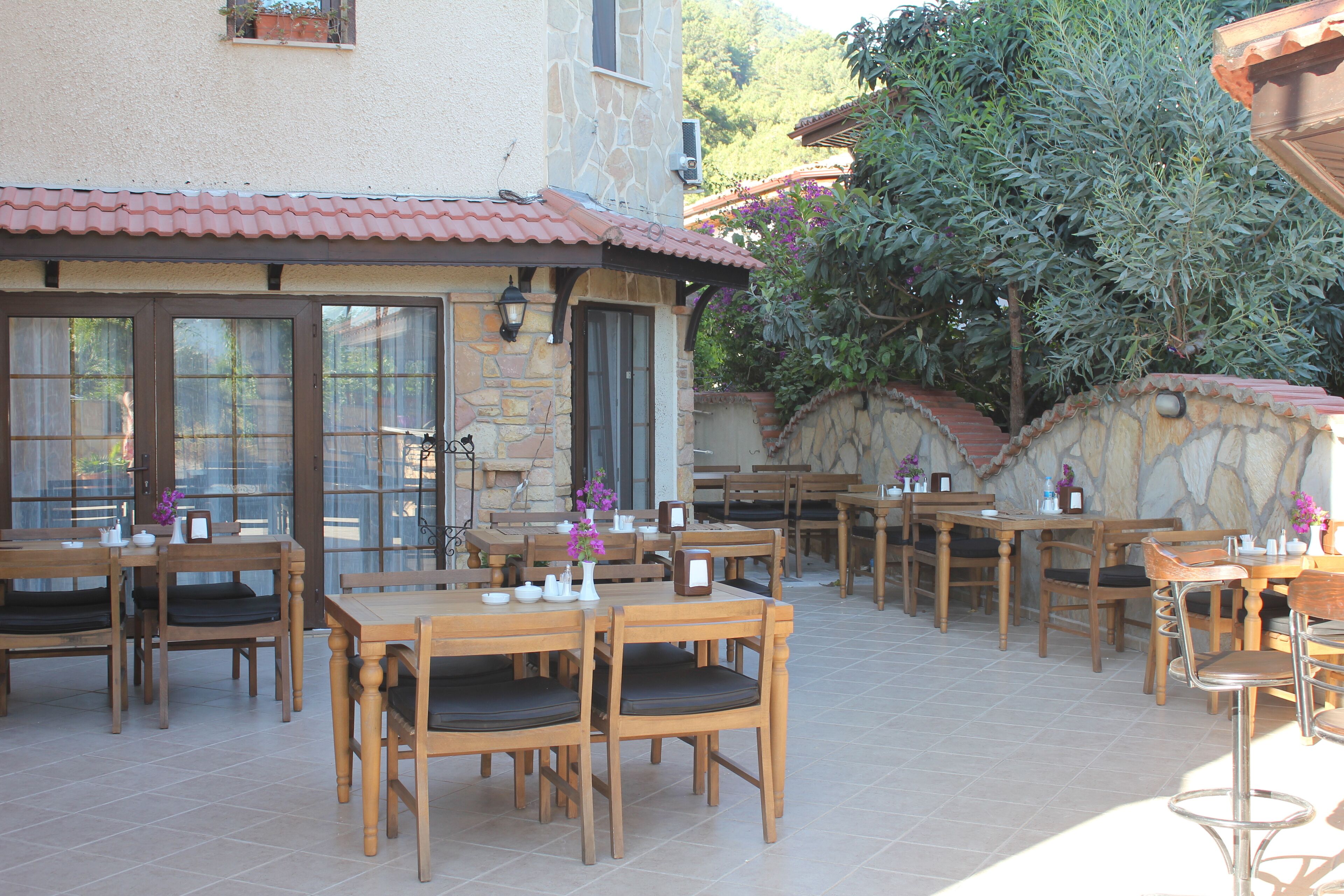 An outdoor patio with wooden tables and chairs, stone walls, and a tiled floor.