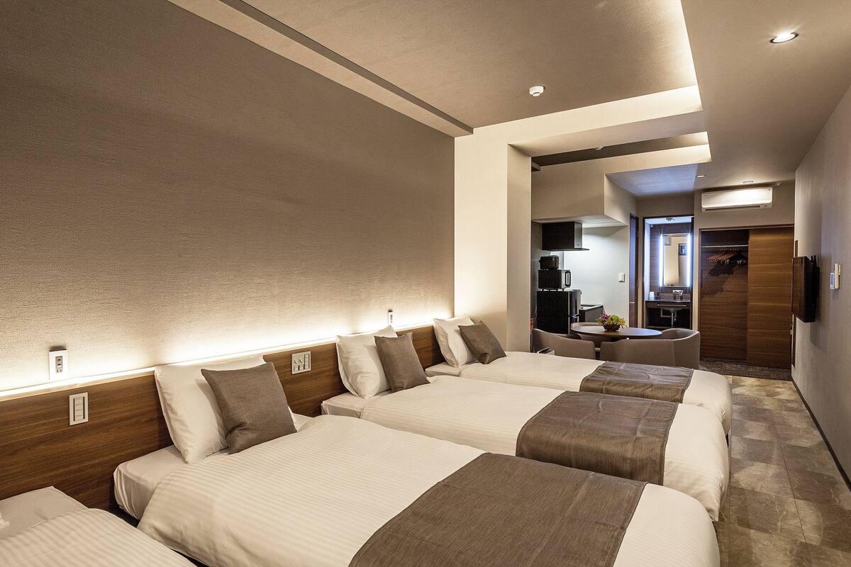 Une chambre d’hôtel avec trois lits, une petite table et un coin cuisine.