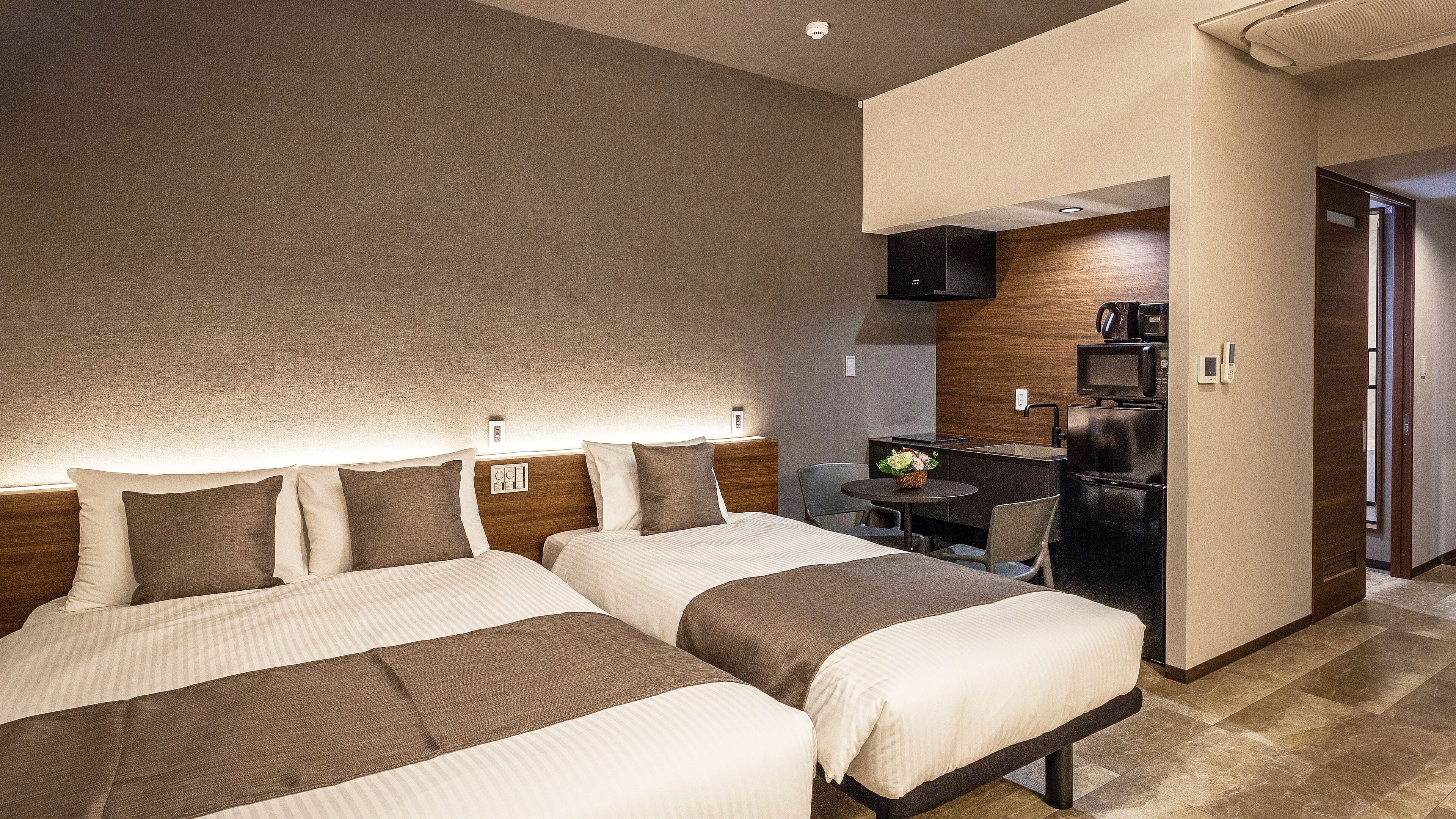 A hotel room with two beds, a small kitchenette, and a dining area.