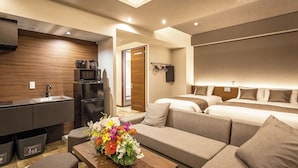 Una habitación de hotel moderna con kitchenette, sofá cama, un panel de madera decorativo y un arreglo floral.