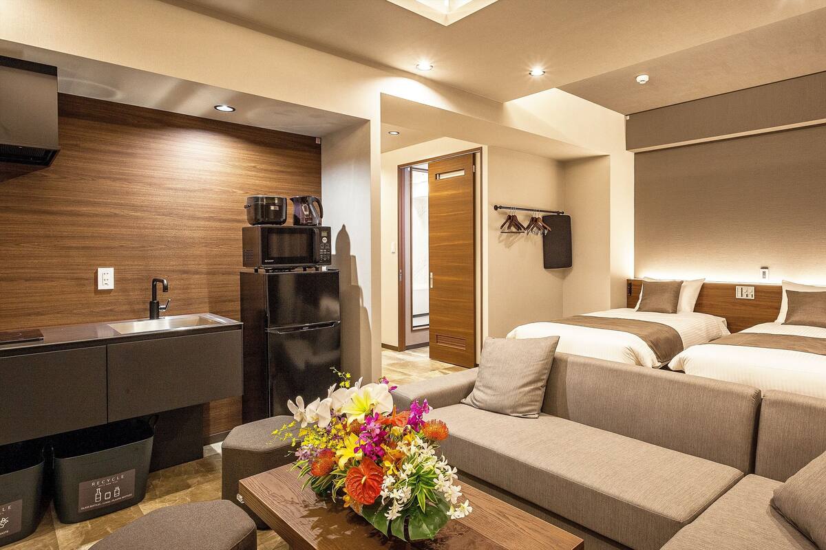 Une chambre d’hôtel moderne dotée d’une kitchenette, d’un canapé-lit, d’un mur décoratif en bois et d’un arrangement floral.