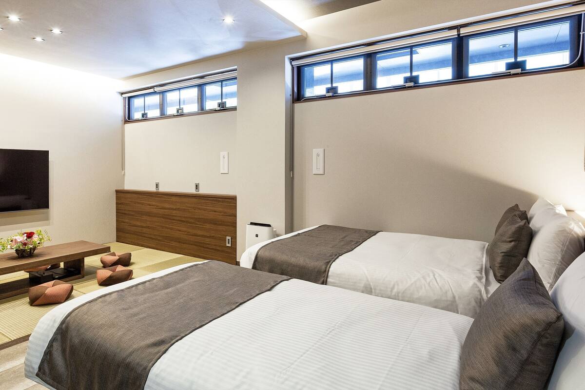 Une chambre d’hôtel avec deux lits, un téléviseur à écran plat, une tête de lit en bois et une petite table sur laquelle est posé un vase de fleurs.
