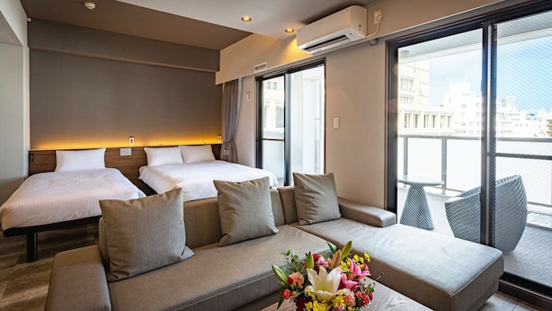 Habitación de hotel con dos camas, un sofá y un balcón con vistas a edificios.
