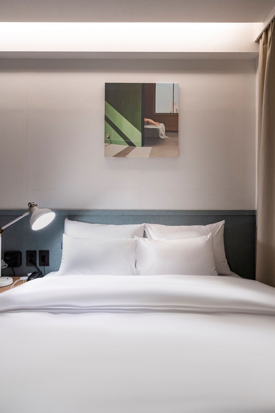Habitació d'hotel amb un llit, una taula de treball amb una làmpada i un quadre a la paret.