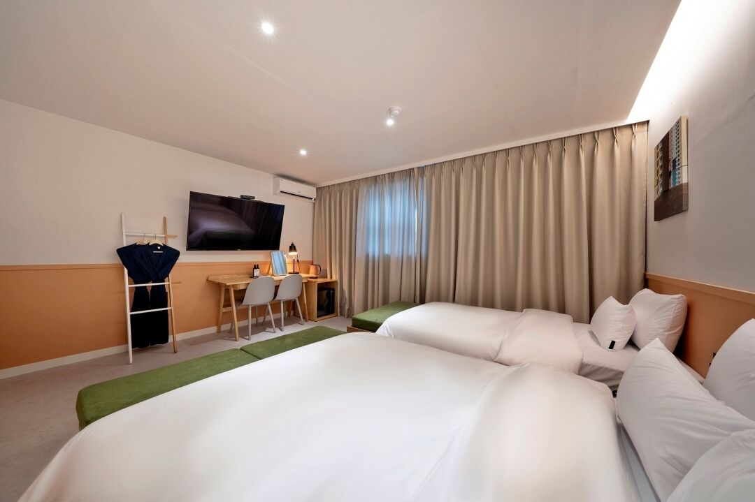 Habitación de hotel con dos camas, un escritorio con silla, televisor y ventana con cortinas.