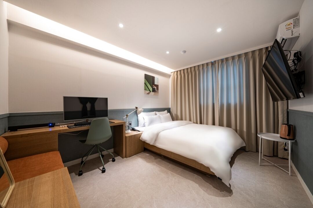 Una habitación de hotel con cama, escritorio, silla, televisor y cortinas.