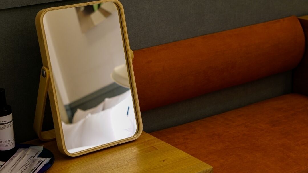 A tablet on a wooden table with a mirror stand, a bottle, and some papers.