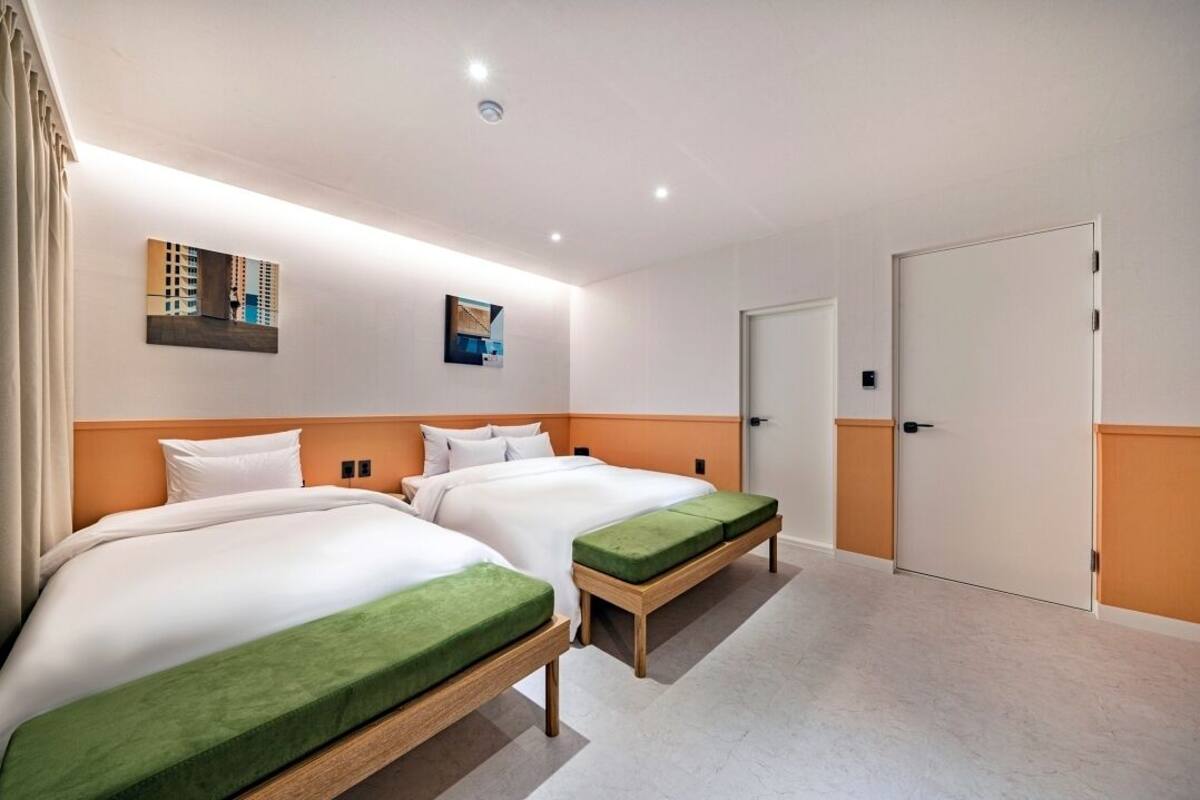 A hotel room with two beds, a door, and artwork on the wall.