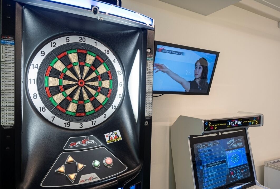 Um alvo de dardos com um visor digital e uma televisão no fundo.